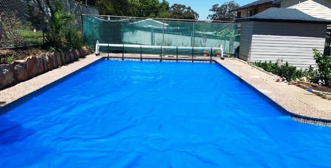 Blue Pool Cover over a swimming pool in a sunny back yard.