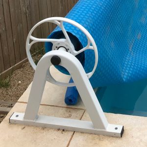 White stationary pool roller with blue pool cover