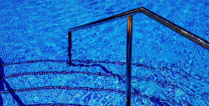 Image is of pool stairs and rail leading into a blue tiled pool