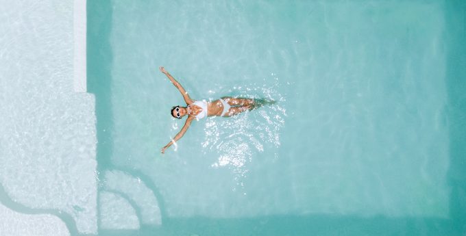 Top view of a woman relaxing in clear pool water on a hot sunny day.